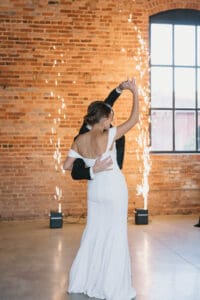 A bride and groom dance in front of a brick wall.
