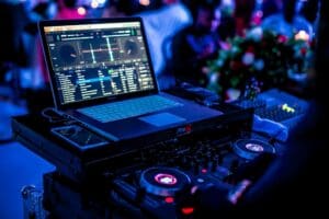 DJ mixing music on a laptop and turntables in a vibrant nightclub.