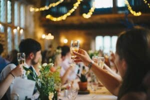 People raising glasses in a festive toast at a warmly lit gathering.
