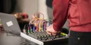 Person adjusting audio mixer with colorful cables connected.